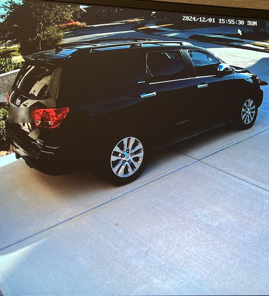 Driveway security camera view of a parked SUV, with the date and time stamped on the footage
