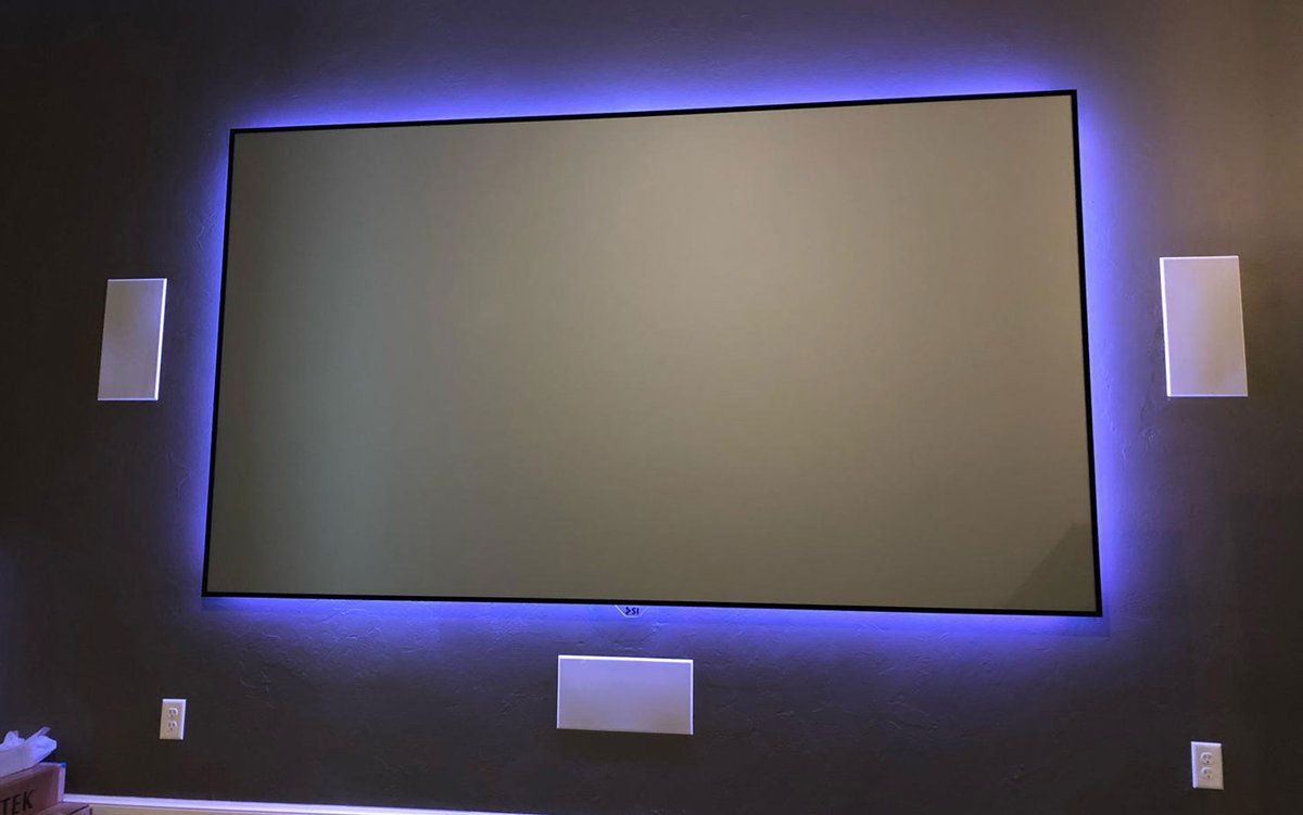 Home theater wall with a backlit projection screen and three in-wall speakers, installed by Starcat Technologies